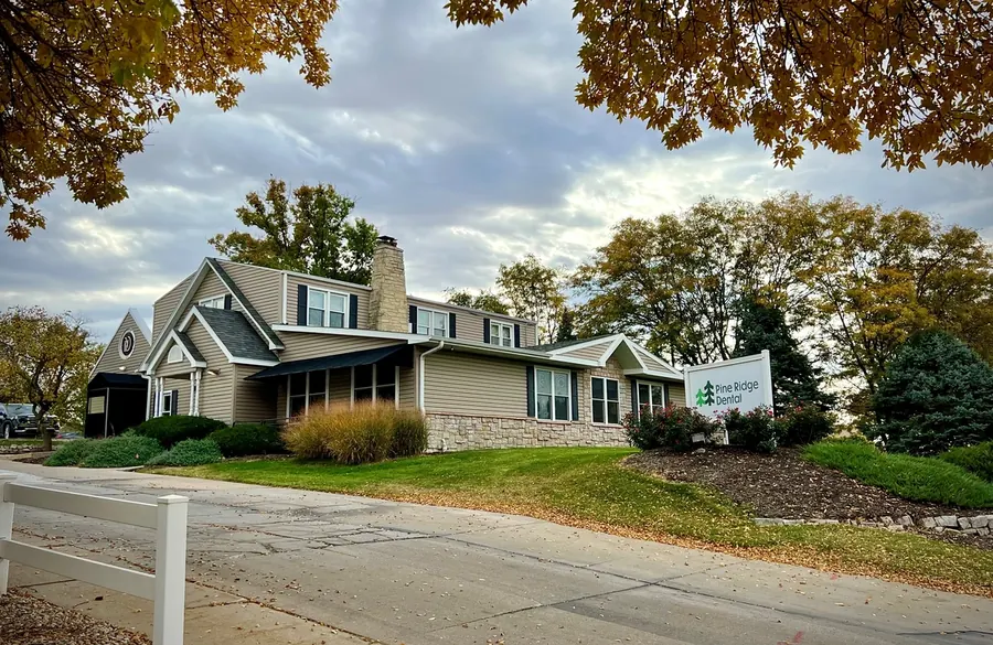 The Edgewood office in autumn, framed by orange leaves, with the Pine Ridge Dental sign on the lawn.